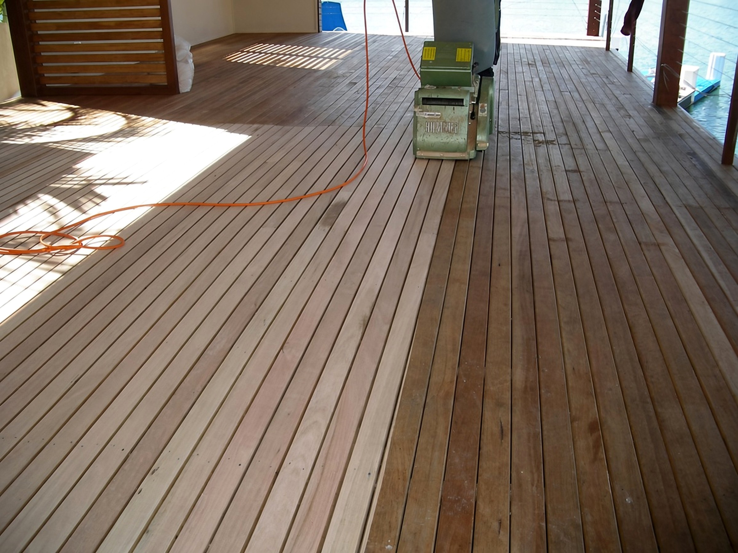 Floor sander on a waterfront timber deck, with the orange power cord shifted slightly left