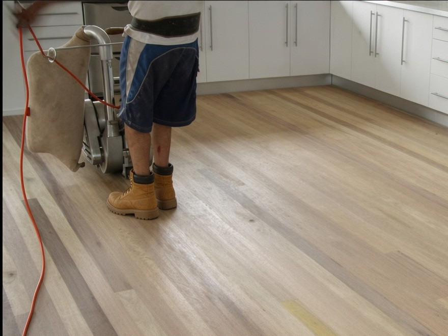 Installer in work boots sanding a newly laid timber floor in a kitchen